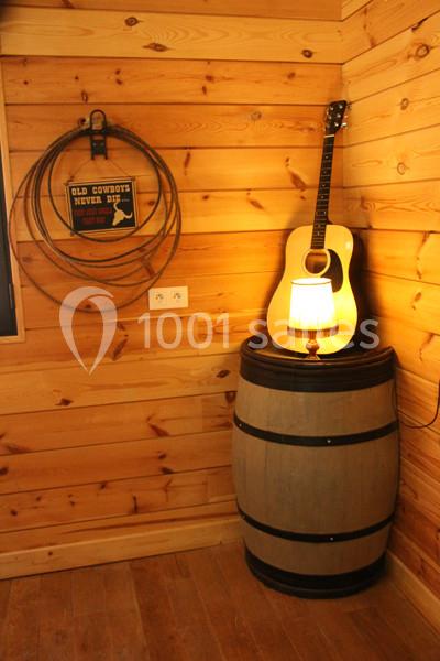 Guitare acoustique posée contre un mur en bois, à côté d'un tonneau surmonté d'une lampe allumée.