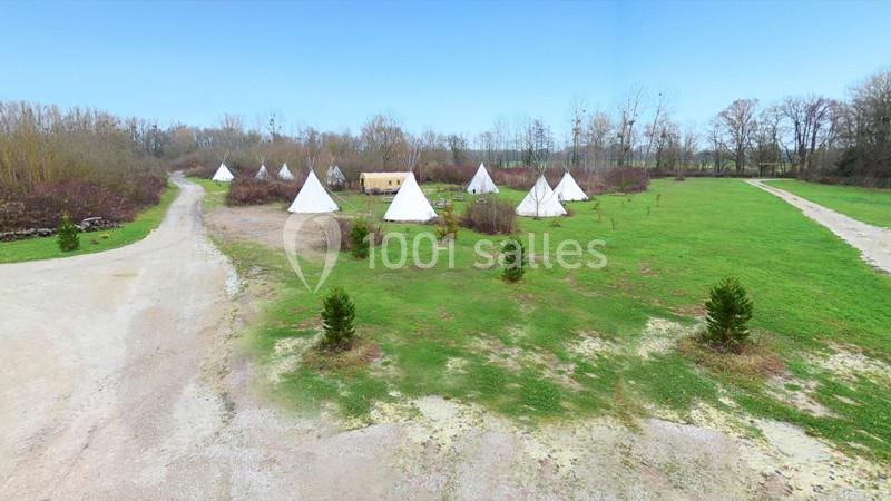 Vue aérienne d'un terrain avec plusieurs tipis blancs dispersés sur une pelouse entourée d'arbres.