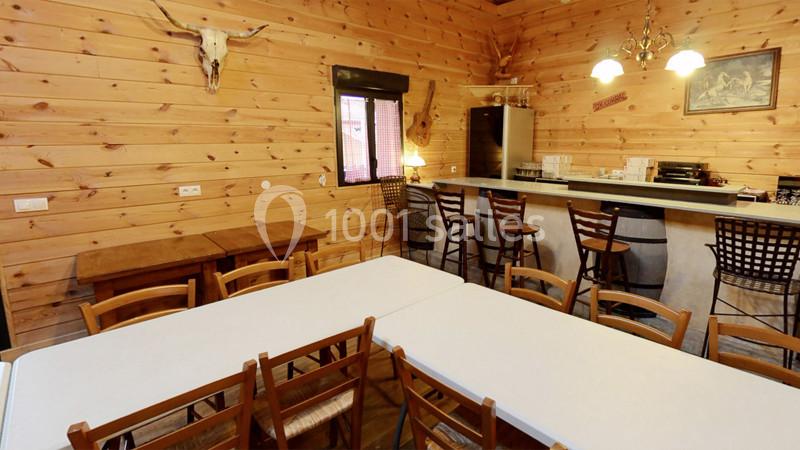 Salle en bois avec tables, chaises, bar équipé de tabourets, décoration rustique et lumière chaleureuse.