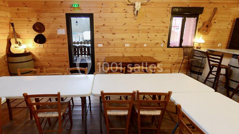 Salle en bois avec tables et chaises, décorée de guitares, chapeaux et tête de cerf accrochée au mur.
