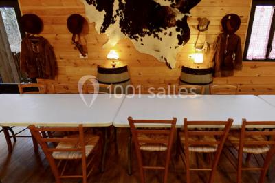 Bâtiments en bois avec une chapelle, une roulotte et des bottes de foin, entourés de verdure.