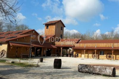 Bâtiments en bois avec une chapelle, une roulotte et des bottes de foin, entourés de verdure.