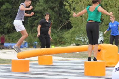 Bâtiments en bois avec une chapelle, une roulotte et des bottes de foin, entourés de verdure.