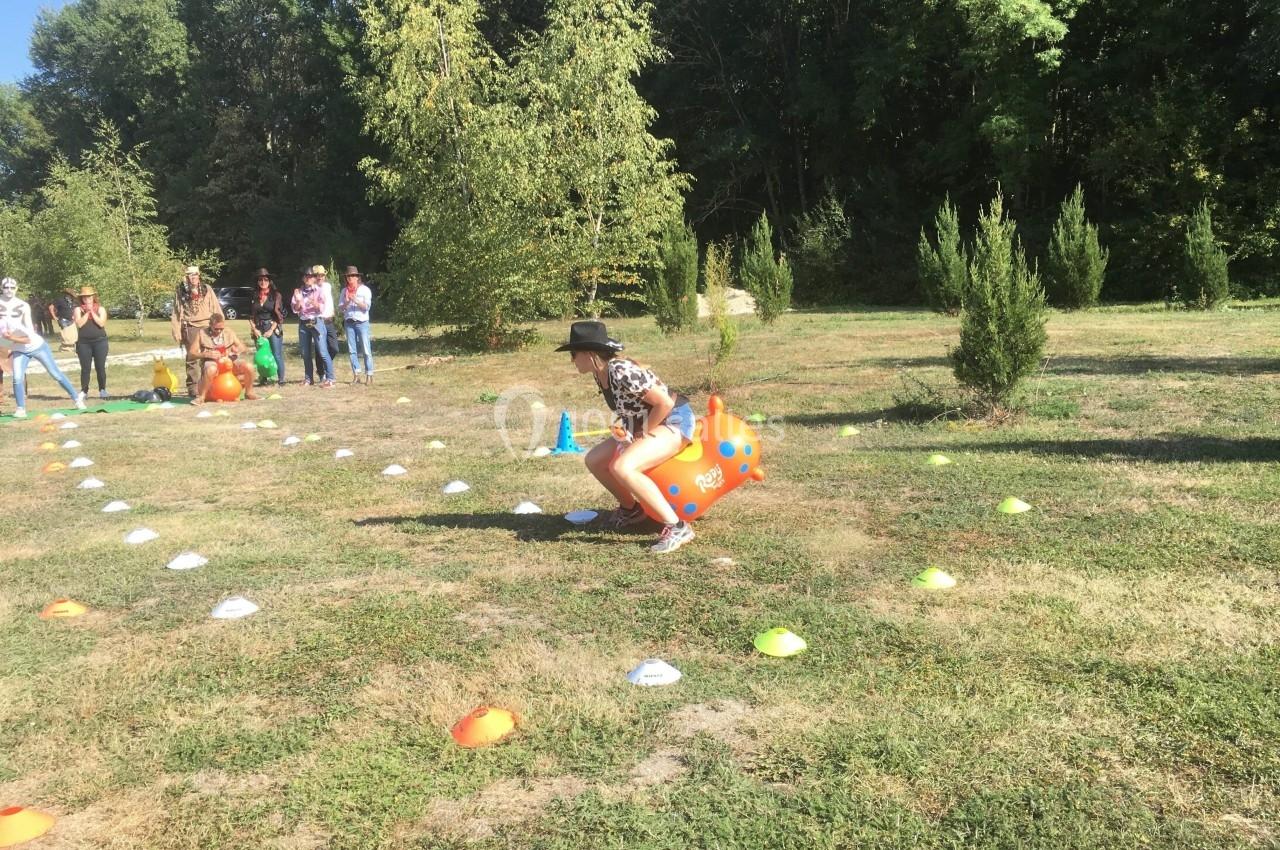 Une personne participe à une course ludique sur un ballon sauteur dans un parc, entourée de spectateurs.