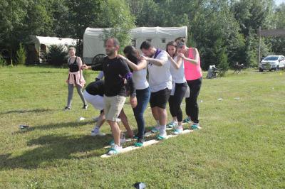 Bâtiments en bois avec une chapelle, une roulotte et des bottes de foin, entourés de verdure.