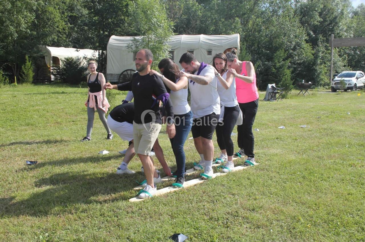 Un groupe de personnes participe à une activité d'équipe en extérieur, debout sur des planches dans un champ.