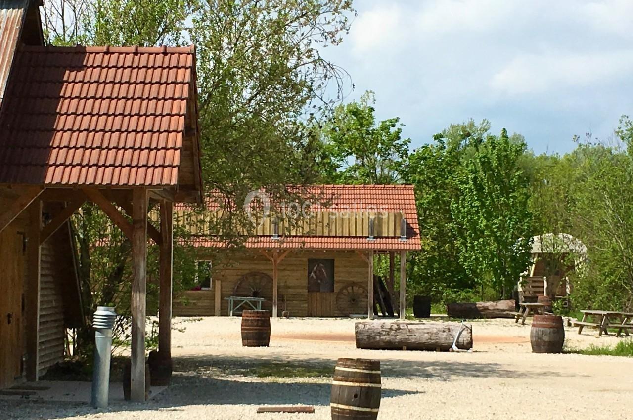 Cour extérieure avec bâtiments en bois, tonneaux, bancs de pique-nique et arbres en arrière-plan.