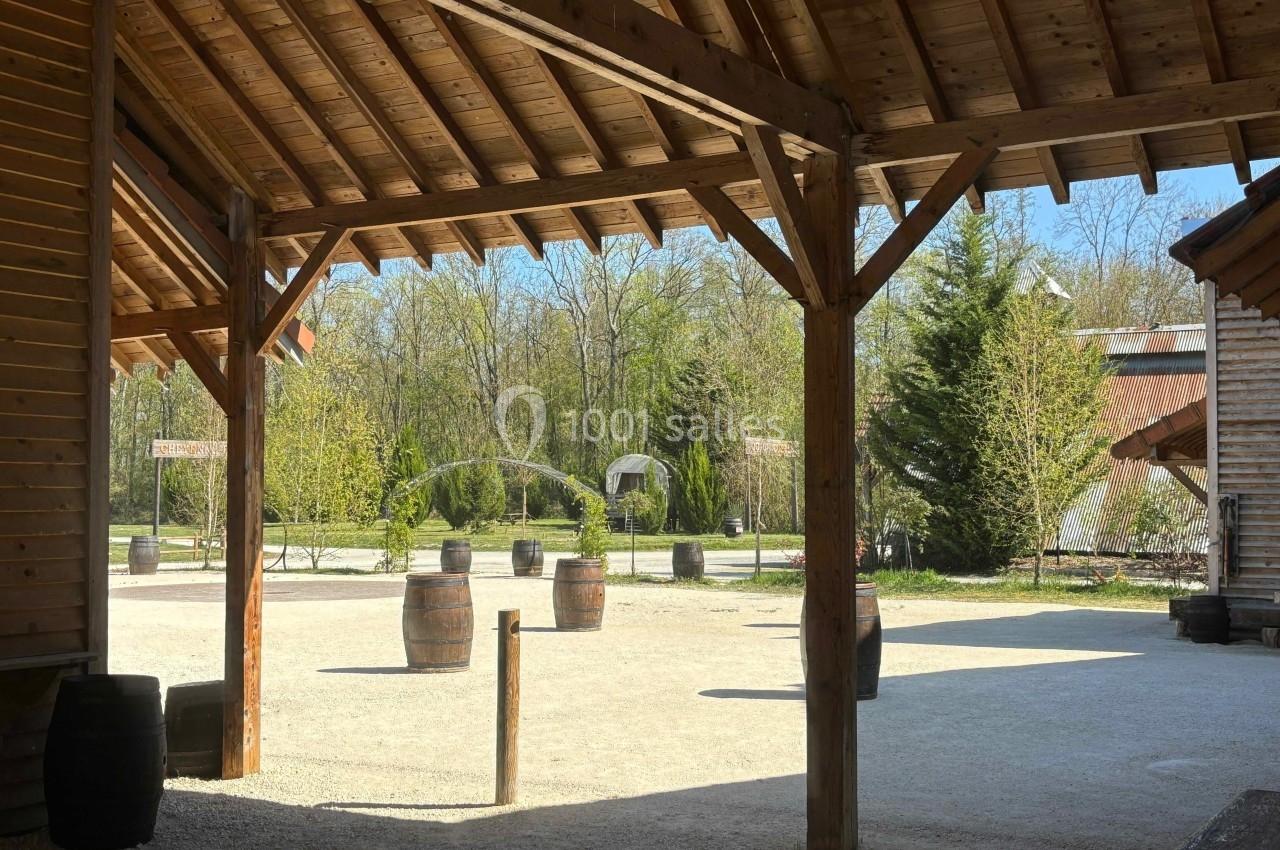 Vue d'une cour extérieure ensoleillée avec des tonneaux en bois dispersés et des bâtiments en bois autour.