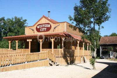Bâtiments en bois avec une chapelle, une roulotte et des bottes de foin, entourés de verdure.
