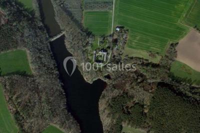 Vue d'un paysage boisé avec un bâtiment en pierre et un toit en ardoise partiellement visible au premier plan.