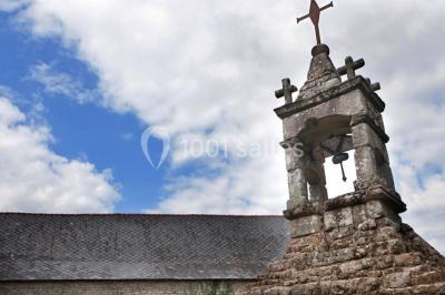 Vue d'un paysage boisé avec un bâtiment en pierre et un toit en ardoise partiellement visible au premier plan.