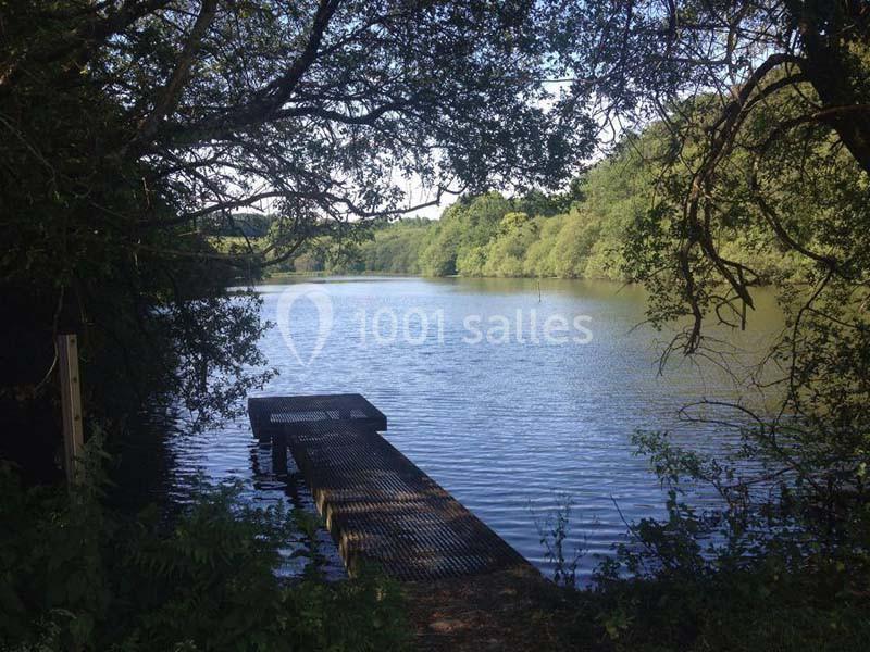 Ponton en bois s'avançant sur un lac entouré d'arbres sous un ciel partiellement dégagé.