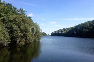Vue d'un paysage boisé avec un bâtiment en pierre et un toit en ardoise partiellement visible au premier plan.