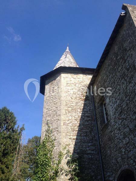 Tour en pierre d'un bâtiment ancien sous un ciel bleu, entourée de végétation et d'arbres.