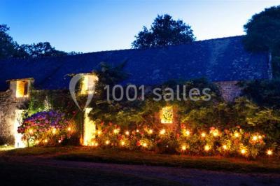 Vue d'un paysage boisé avec un bâtiment en pierre et un toit en ardoise partiellement visible au premier plan.