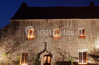 Vue d'un paysage boisé avec un bâtiment en pierre et un toit en ardoise partiellement visible au premier plan.