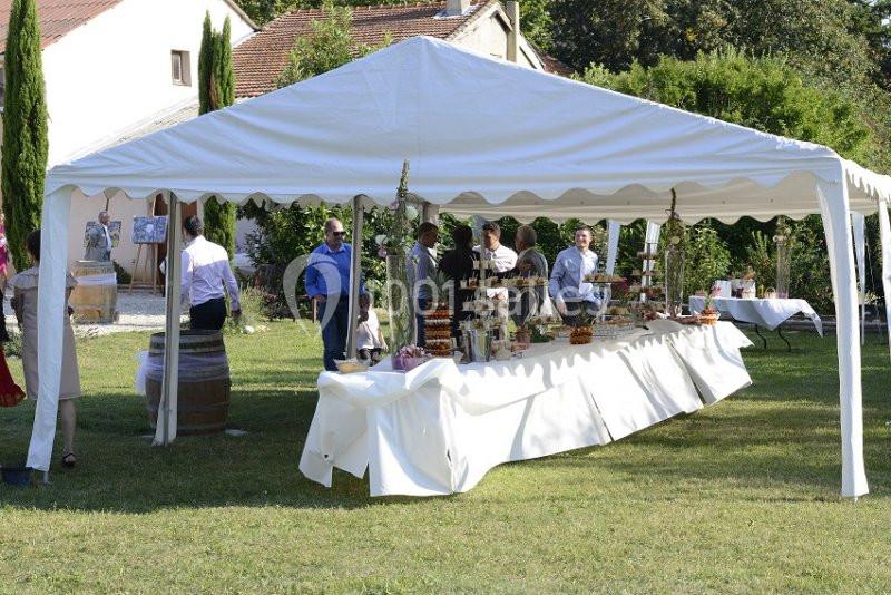 Tente blanche installée dans un jardin, abritant un buffet avec plusieurs personnes en train de se servir.