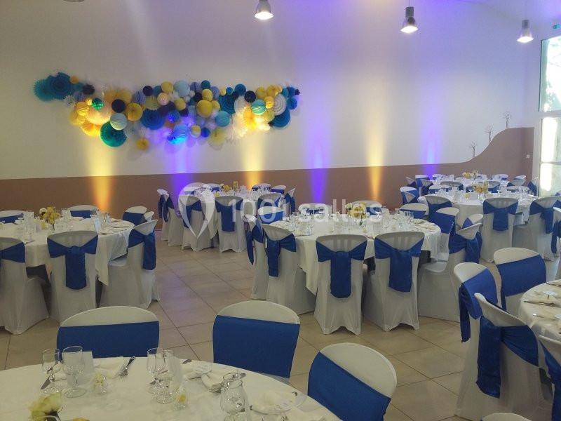 Salle de réception décorée avec des tables dressées, des nappes blanches et des chaises ornées de nœuds bleus.