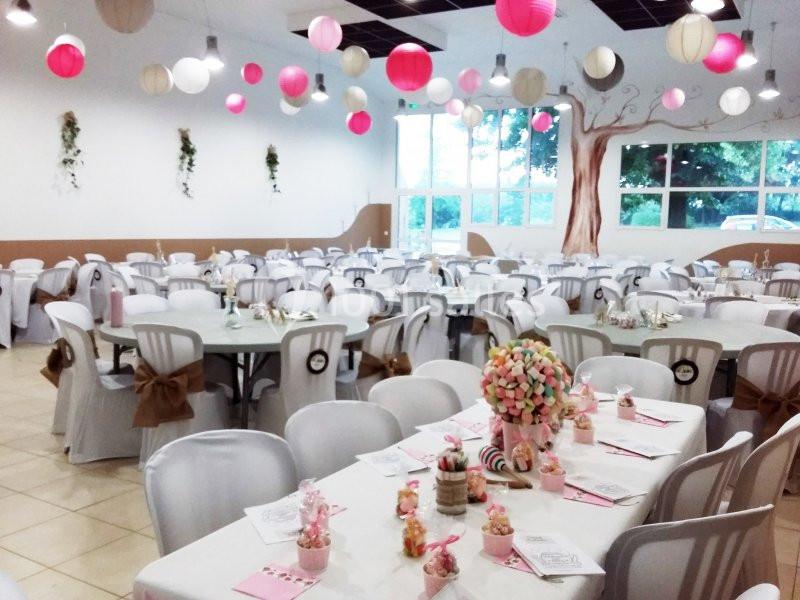 Salle décorée pour une réception avec tables dressées, chaises blanches et lanternes suspendues roses et blanches.