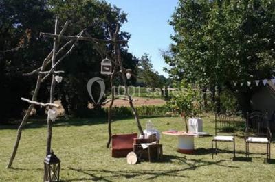 Mobilier en palettes décoré de tissu blanc et de fleurs roses, disposé dans un jardin ombragé.