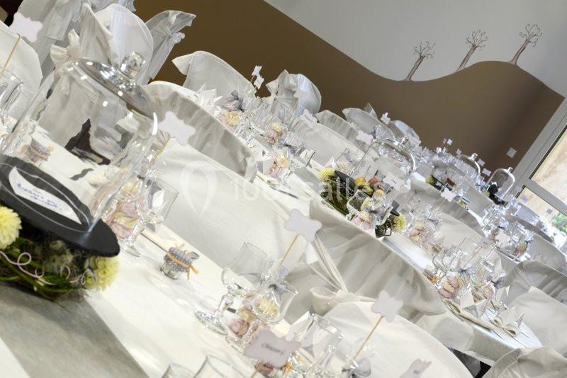 Salle de réception décorée avec des tables blanches, des cloches en verre et des centres de table fleuris.
