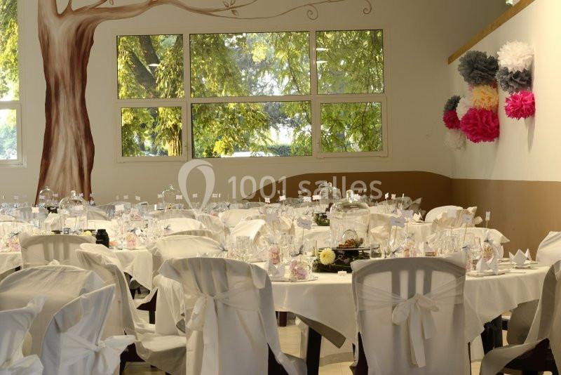 Salle décorée pour un événement avec des tables dressées, des chaises couvertes de housses blanches et des décorations…
