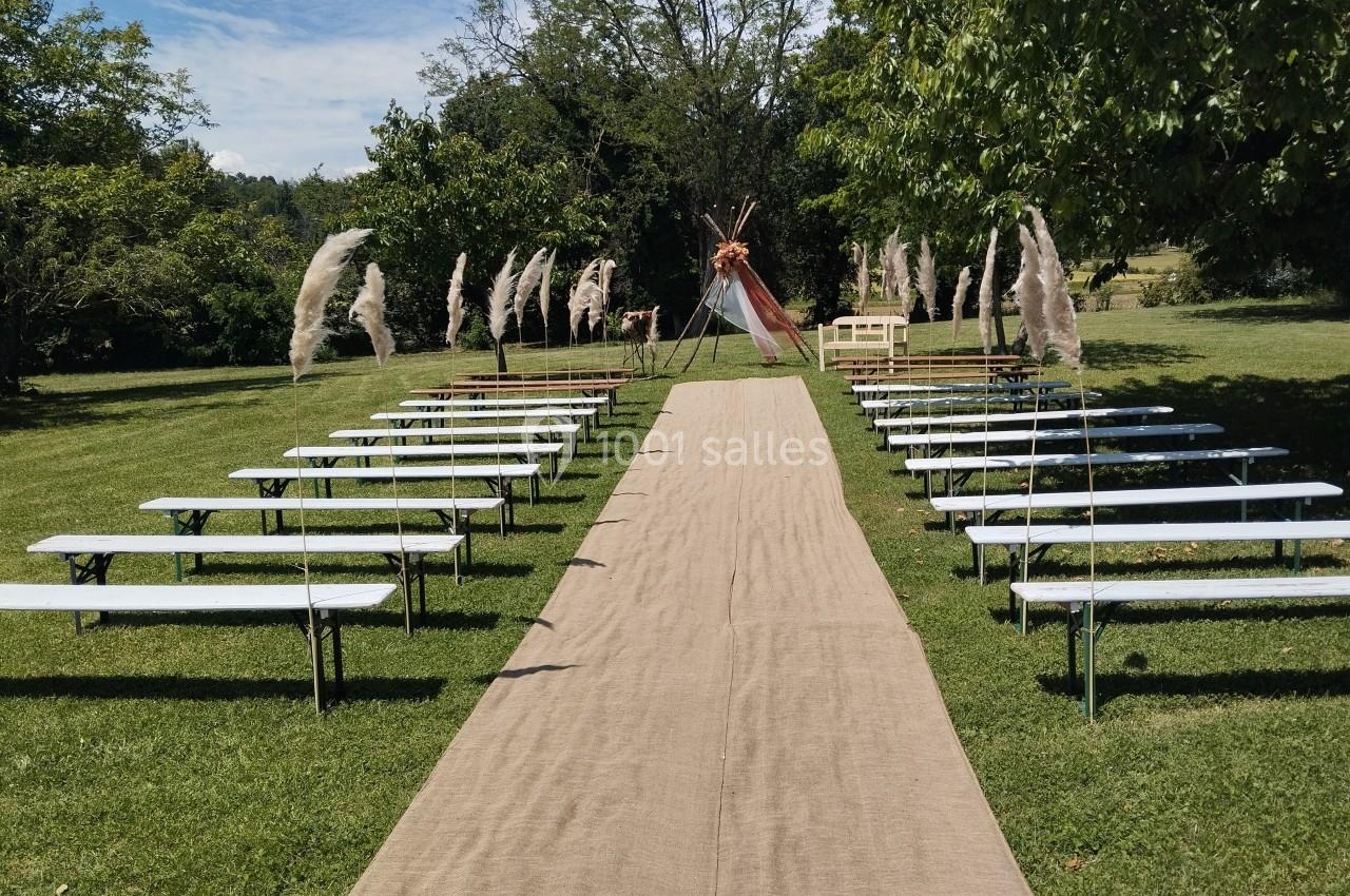 Allée centrale bordée de bancs en bois, menant à une arche décorée, dans un jardin verdoyant.