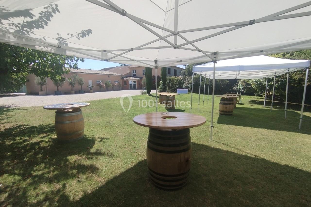 Tables rondes en tonneaux disposées sous des tonnelles blanches dans un jardin ensoleillé.