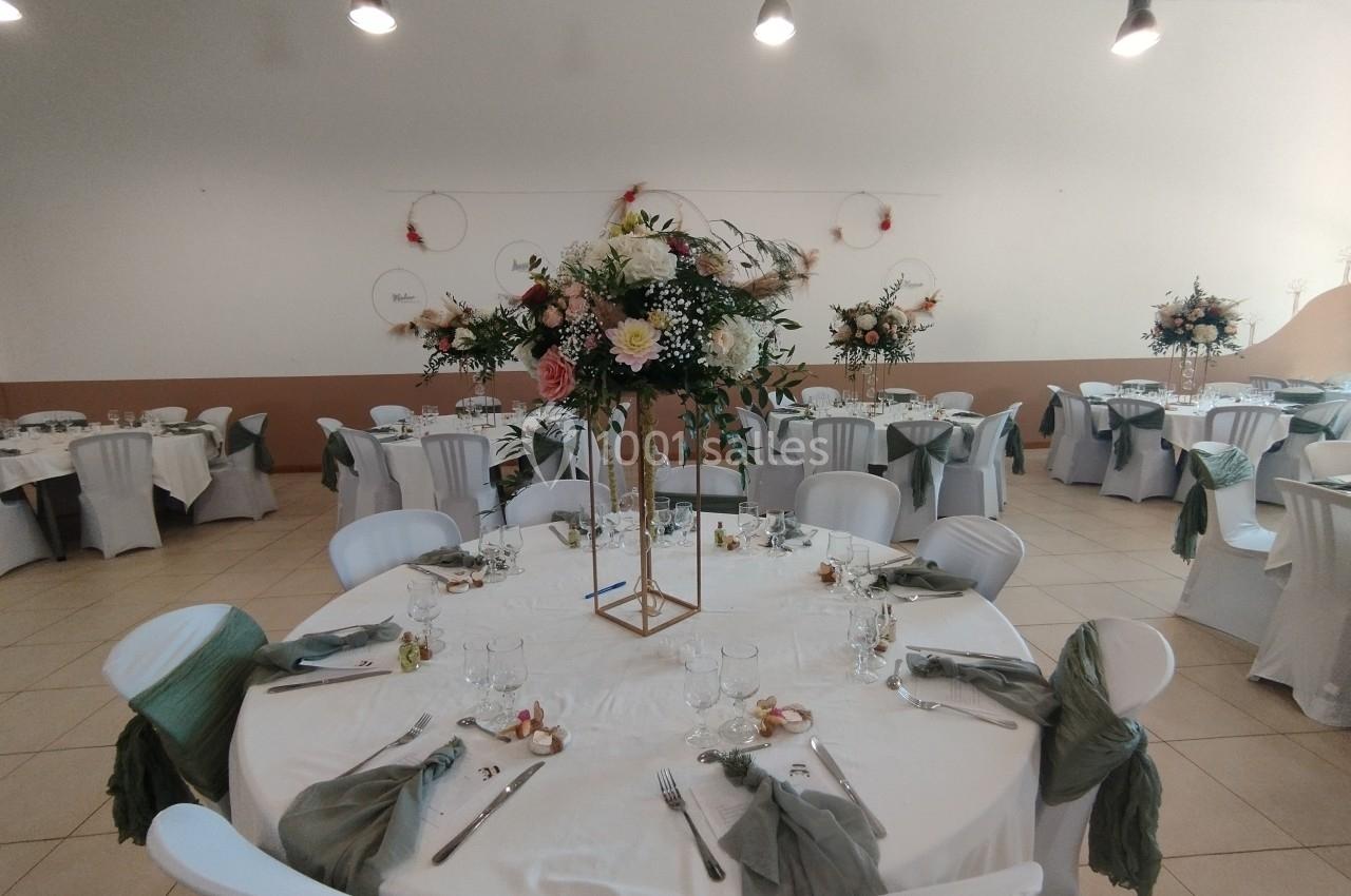 Salle de réception décorée avec des tables rondes, nappes blanches, chaises habillées et centres de table floraux.