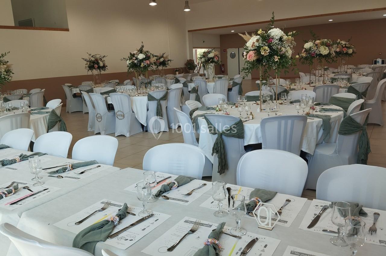 Salle de réception décorée avec des tables rondes et rectangulaires, nappes blanches, chaises ornées de nœuds verts et…