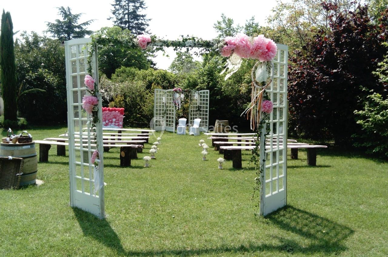 Allée de jardin décorée pour une cérémonie en plein air, avec bancs en bois, fleurs et arche ornée de roses.