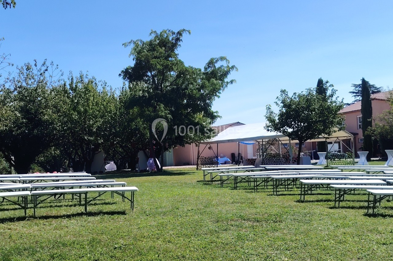 Des bancs alignés sur une pelouse verte, entourés d'arbres et de tentes blanches, par une journée ensoleillée.