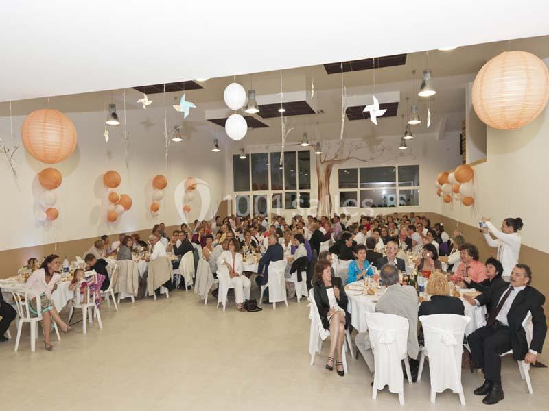 Salle décorée avec des lanternes et des ballons, remplie de personnes assises à des tables lors d'un événement.