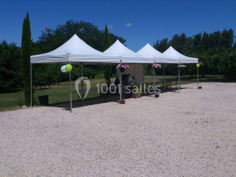 Trois tentes blanches alignées sur un sol gravillonné, entourées de verdure et décorées de fleurs suspendues.