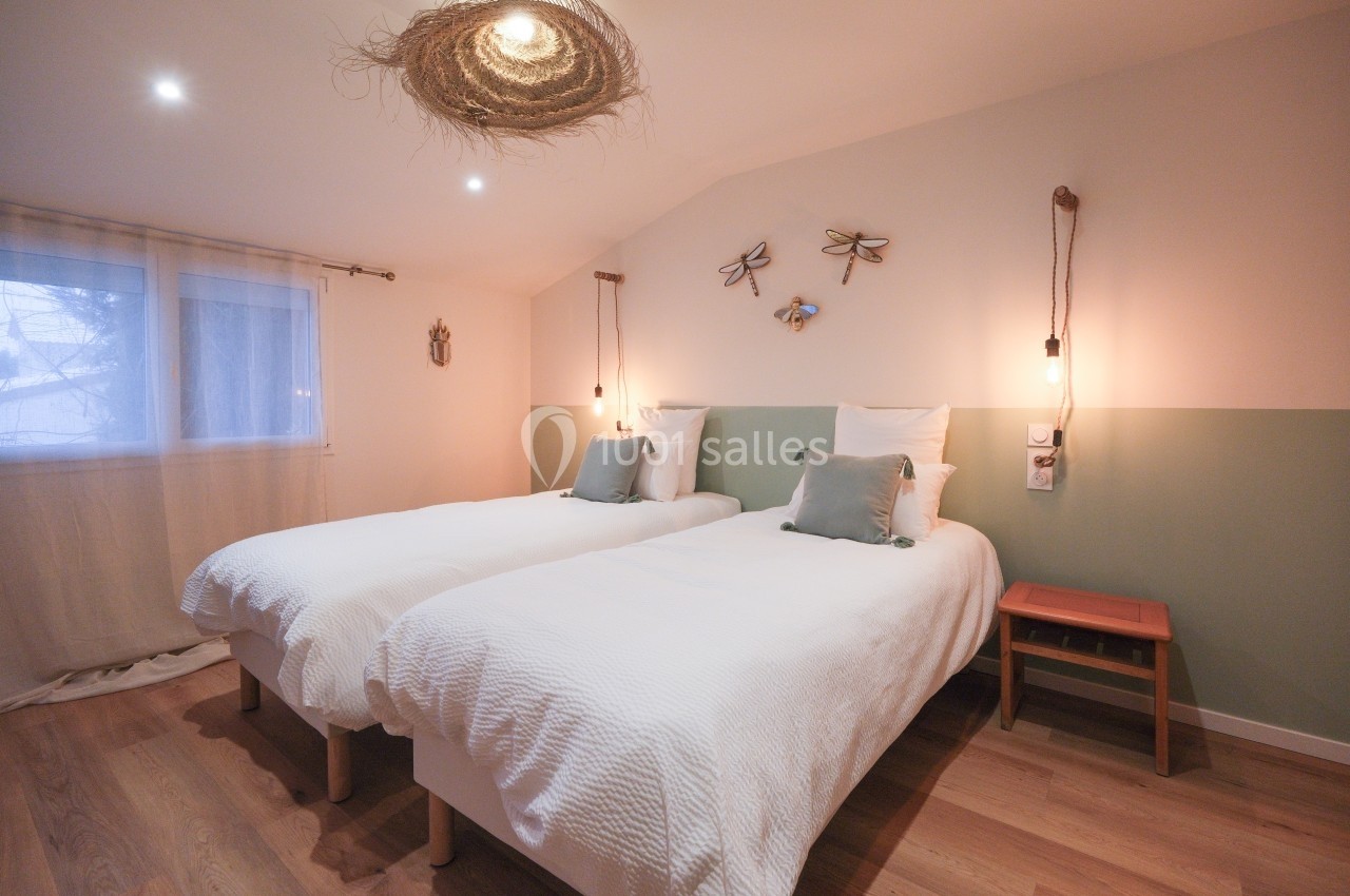 Deux lits simples avec linge blanc dans une chambre lumineuse, décorée de tons pastel et d'éléments naturels.