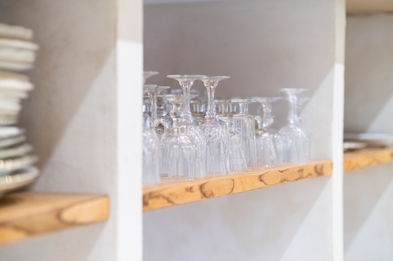 Verres à pied transparents alignés sur une étagère en bois dans un espace de rangement lumineux.