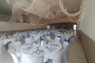 Salle décorée pour un événement, avec tables dressées, nappes noires, centres de table à plumes blanches et ballons dorés.