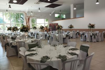 Salle décorée pour un événement, avec tables dressées, nappes noires, centres de table à plumes blanches et ballons dorés.