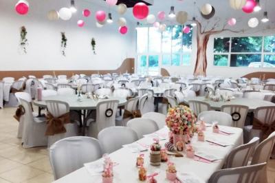 Salle décorée pour un événement, avec tables dressées, nappes noires, centres de table à plumes blanches et ballons dorés.