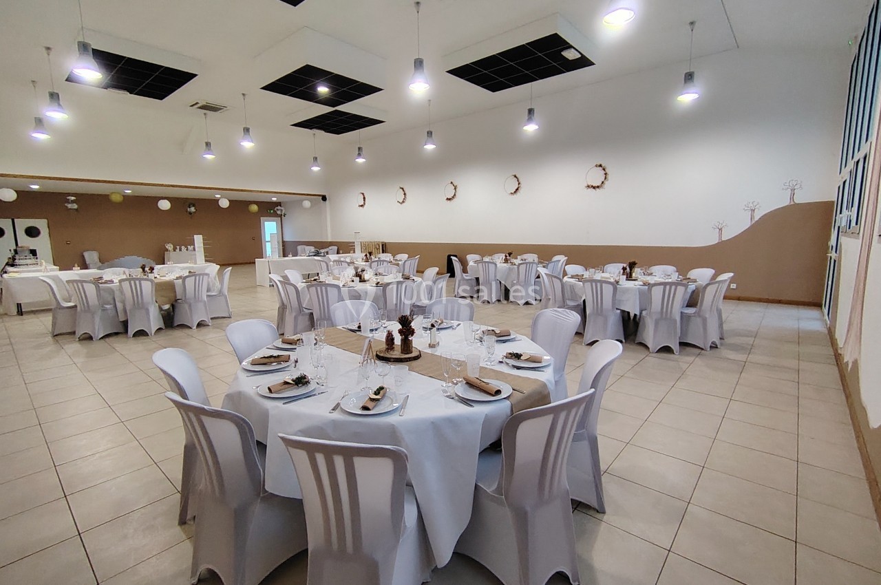 Salle de réception décorée avec des tables rondes dressées, nappes blanches et chaises assorties.