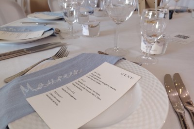 Salle décorée pour un événement, avec tables dressées, nappes noires, centres de table à plumes blanches et ballons dorés.