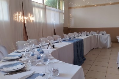 Salle décorée pour un événement, avec tables dressées, nappes noires, centres de table à plumes blanches et ballons dorés.