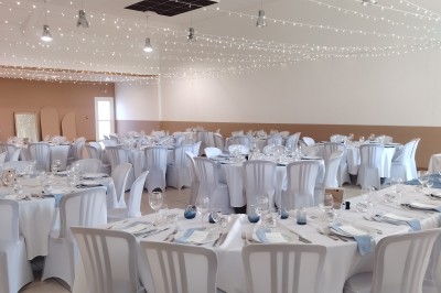 Salle décorée pour un événement, avec tables dressées, nappes noires, centres de table à plumes blanches et ballons dorés.