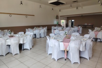 Salle décorée pour un événement, avec tables dressées, nappes noires, centres de table à plumes blanches et ballons dorés.