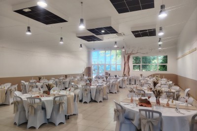 Salle décorée pour un événement, avec tables dressées, nappes noires, centres de table à plumes blanches et ballons dorés.
