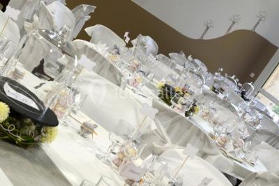 Salle décorée pour un événement, avec tables dressées, nappes noires, centres de table à plumes blanches et ballons dorés.