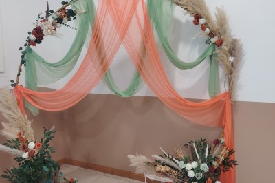 Salle décorée pour un événement, avec tables dressées, nappes noires, centres de table à plumes blanches et ballons dorés.