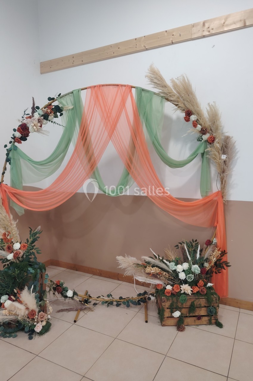 Arche décorative ornée de voilages orange et verts, fleurs séchées et feuillages, posée dans une salle claire.