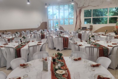 Salle décorée pour un événement, avec tables dressées, nappes noires, centres de table à plumes blanches et ballons dorés.