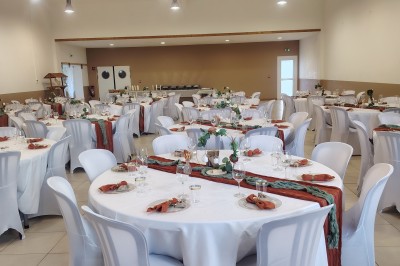 Salle décorée pour un événement, avec tables dressées, nappes noires, centres de table à plumes blanches et ballons dorés.